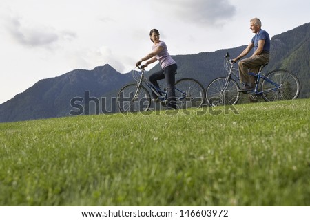 Side view of a middle aged man and woman biking on landscape with mountain range in the background