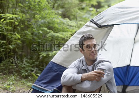 Thoughtful and relaxed young man sitting by tent