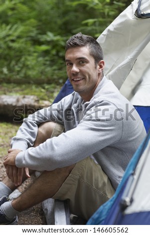 Side view portrait of a smiling young man sitting by tent