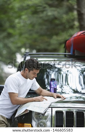 Side view of a young man reading map on car bonnet