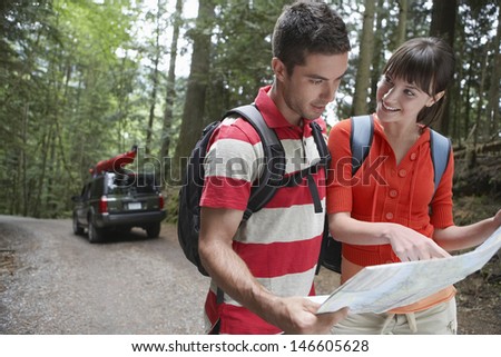 Smiling young couple with map on forest road with SUV in the background