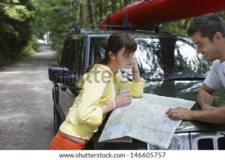 Side view of a young couple looking at map on car bonnet in the forest