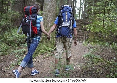 Rear view of a young couple with backpacks holding hands and walking in forest