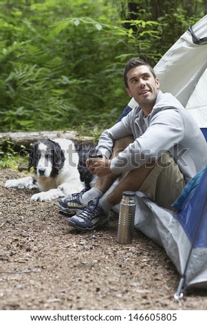 Side view of a young man sitting by tent with dog