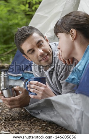 Side view of a young couple with drinks lying in tent entrance