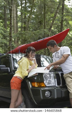 Side view of a young couple looking at map on car bonnet in the forest