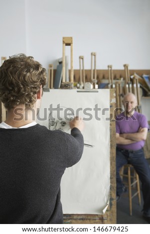 Rear view of a male artist drawing charcoal portrait of model in studio