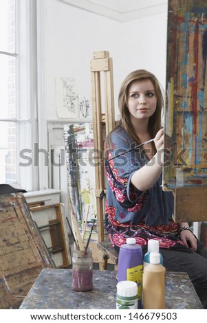 Young female artist painting at easel in art studio
