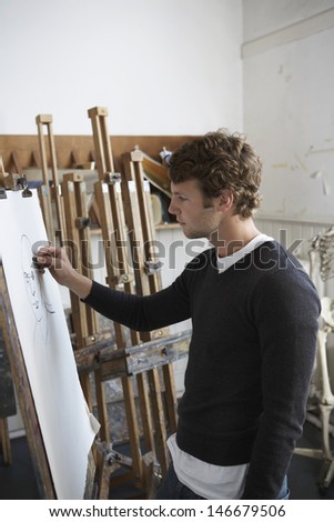 Side view of a male artist drawing charcoal portrait in studio