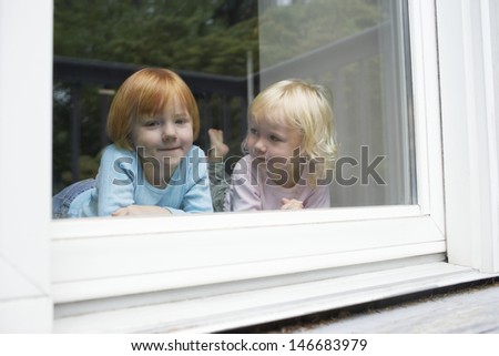Portrait of cute girl lying with sister in front of glass window at home