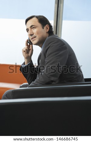 Side view of middle aged businessman using mobile phone in office lobby