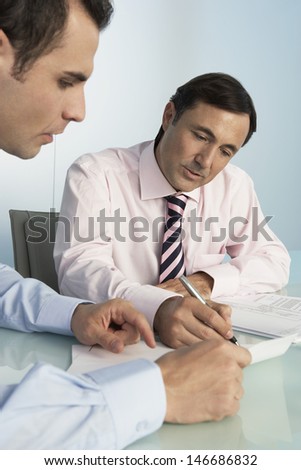 Middle aged businessman discussing over document with male colleague at desk in office
