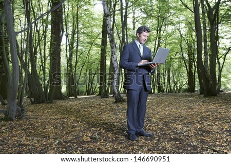 Full length of businessman using laptop in middle of forest