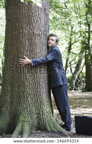 Side view of businessman with eyes closed embracing tree trunk in forest