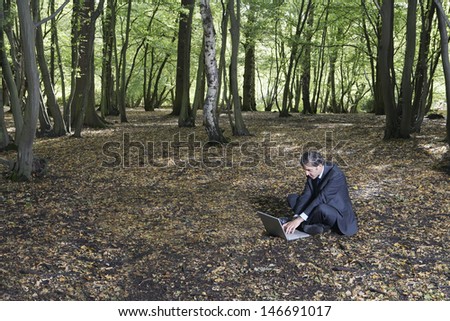 Businessman using laptop while sitting on land in forest