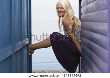 Side view portrait of happy young woman sitting on balustrade of beach cabin