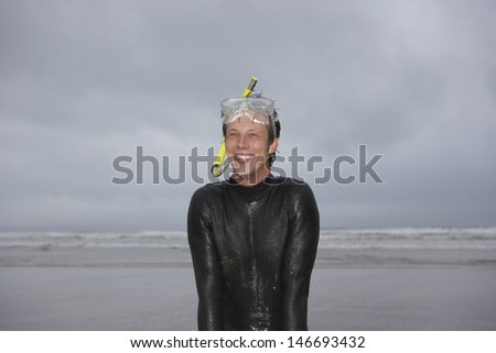 Happy young man wearing snorkel and mask looking away while standing on beach