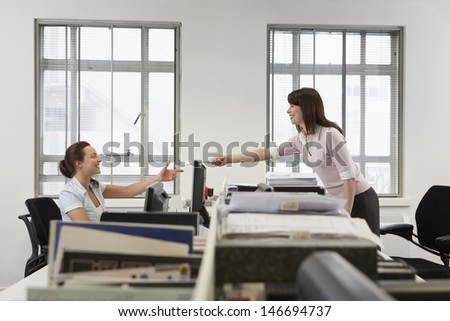 Side view of young businesswoman passing document to colleague over desk in office