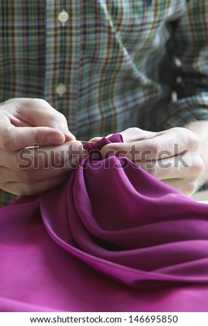Midsection closeup of male tailor sewing fabric at table