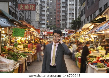 Portrait of handsome young businessman using cell phone at street market