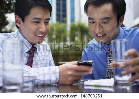 Two young businessmen reading text message on cell phone at outdoor cafe