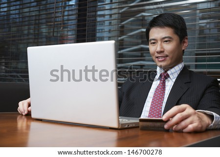 Handsome young businessman using laptop and credit card at restaurant table