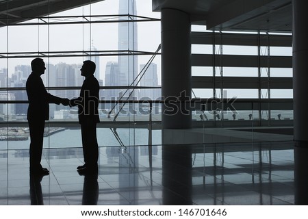 Full Length Side View Of Businessmen Shaking Hands In Airport Terminal