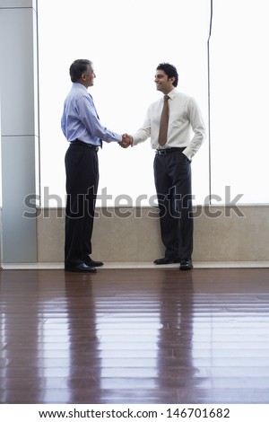 Full length of businessmen shaking hands in office
