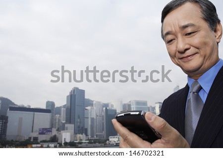 Middle aged businessman reading text message on cell phone with cityscape in background