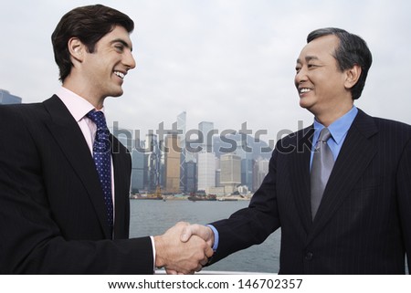 Two Businessmen Shaking Hands With Cityscape In Background