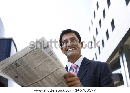 Happy young businessman reading newspaper outside office building