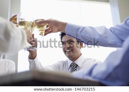 Happy young businessman with colleagues toasting wineglasses in restaurant
