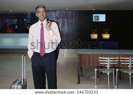 Portrait of happy middle aged businessman with luggage in hotel lobby