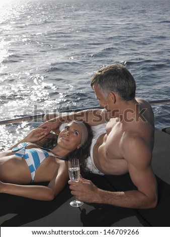 Loving couple with champagne flute relaxing at the edge of yacht by sea