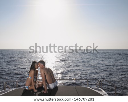 Romantic couple rubbing noses while sitting on yacht\'s edge by sea