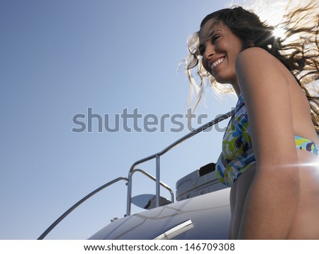 Low angle view of happy woman standing on yacht against clear sky