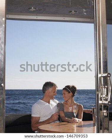 Loving couple with champagne flutes sitting at table on yacht