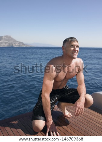 Middle aged man looking away while crouching on yacht\'s floorboard