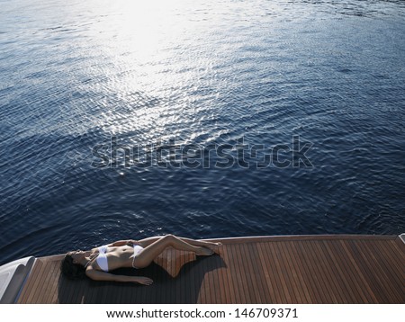 High angle view of woman in bikini sunbathing on yacht\'s floorboard by sea