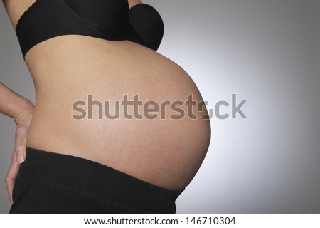 Midsection of pregnant woman with hand on her back on gray background