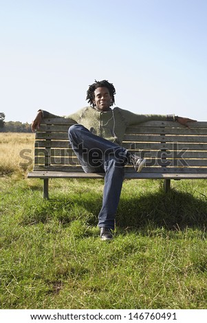Full length of young man listening to music while sitting on park bench