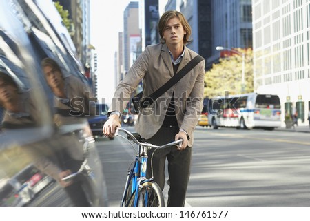 Portrait of handsome young businessman with bicycle on busy street