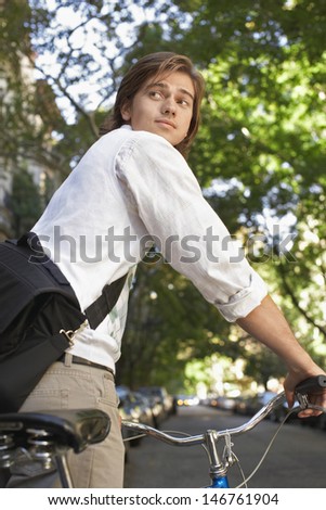 Young businessman with bicycle looking over shoulder on city street