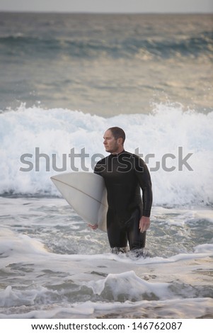 Male surfer carrying surfboard while walking back from sea