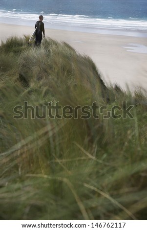 Rear view of male surfer carrying surfboard on beach looking at sea