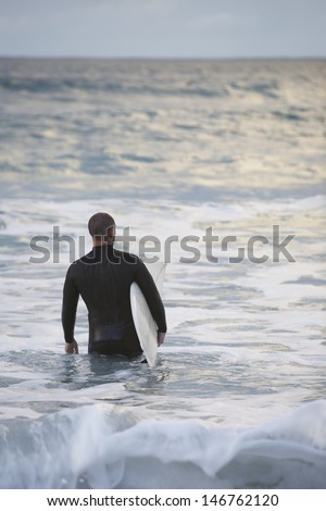 Rear view of male surfer carrying surfboard into sea
