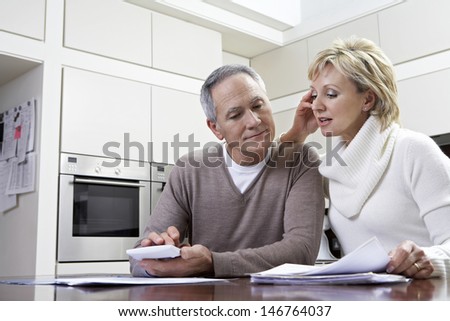 Middle aged couple making calculations using calculator at kitchen table