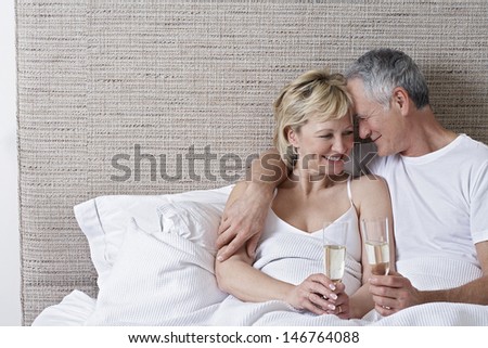 Romantic middle aged couple holding champagne flutes in bed
