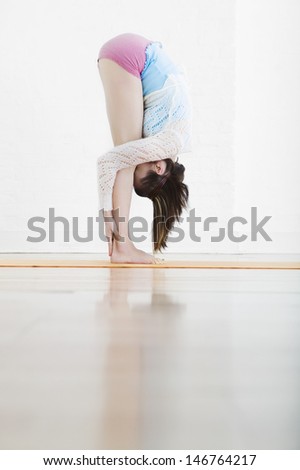 Profile shot of woman doing Standing Forward Bend in gym