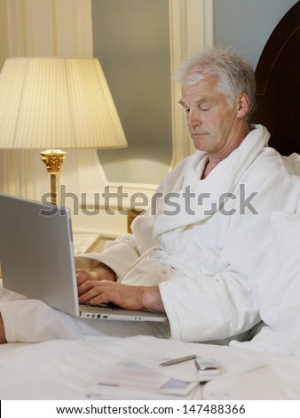 Middle aged man in bathrobe using laptop in bed